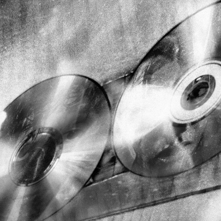 Single artwork for TOWNS' Magnificant featuring a close-up black-and-white image of two reflective CDs side by side with eye-like centers.